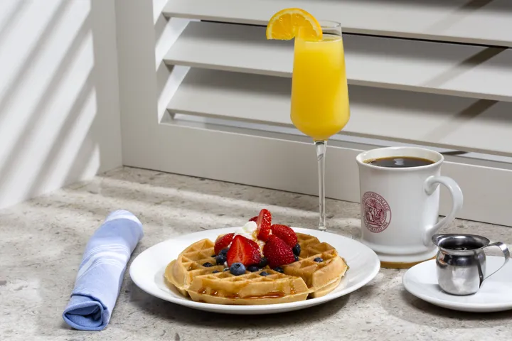 Waffle on a plate with berries on top and a mimosa and coffee